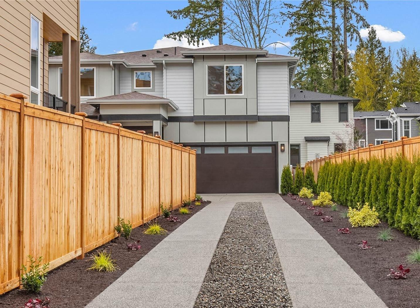 Modern two-story house exterior with a two-car garage, large windows, dark garage door, and wood fence.