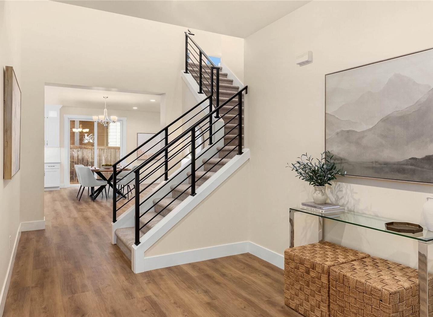 Interior view of a two-story home entrance with wood flooring, a modern staircase with black railings, and view into dining area.