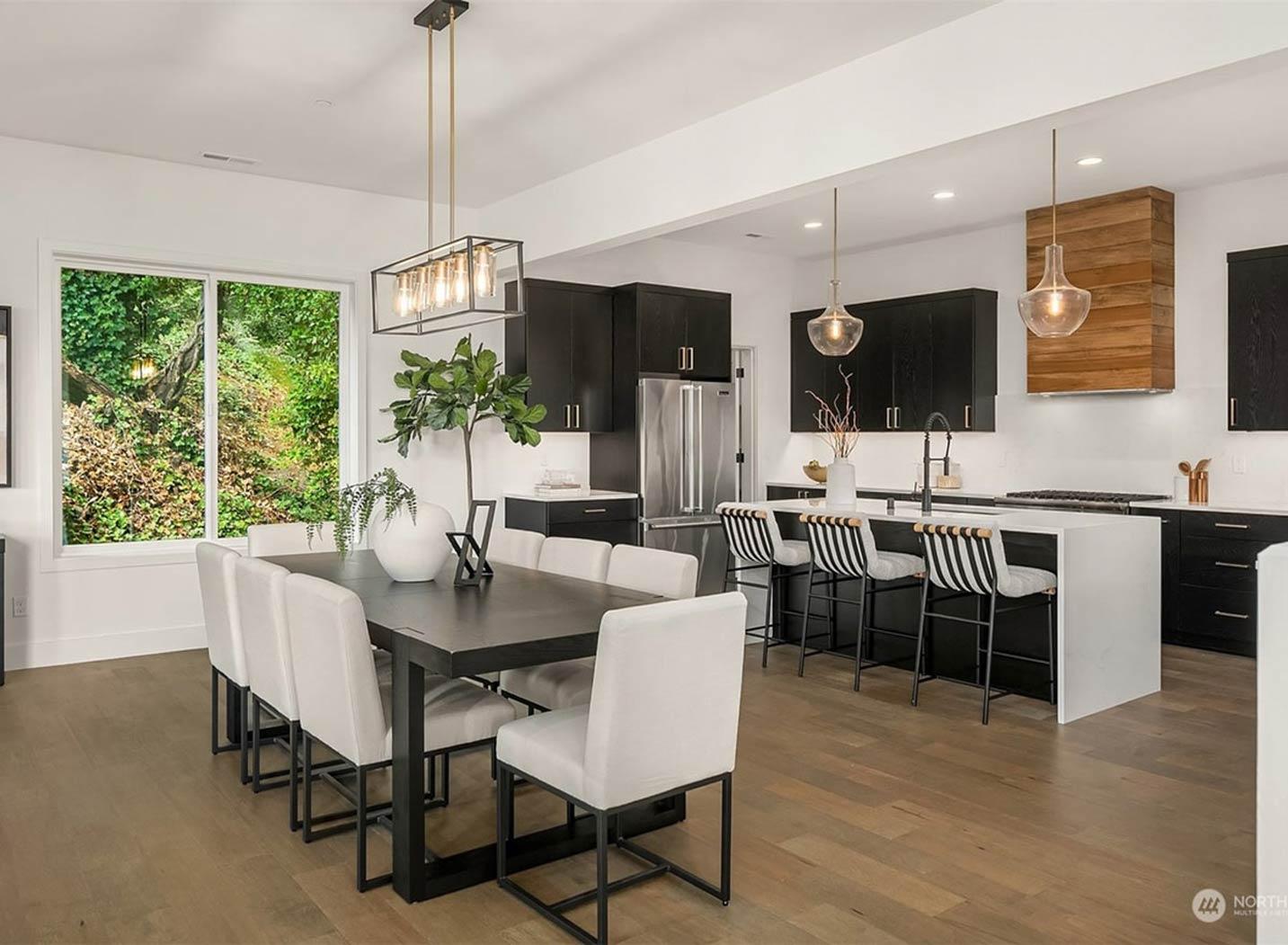 Open concept kitchen and dining area with dark cabinets, island seating, and large window overlooking greenery.