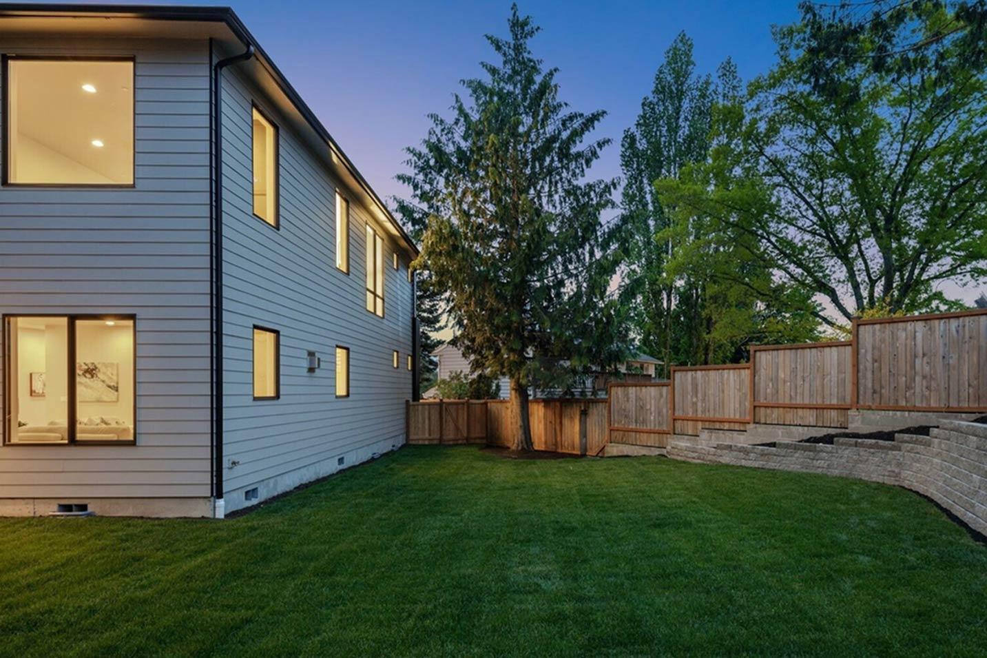 Modern two-story house exterior with horizontal siding, large windows, and a tiered wooden fence in the backyard.