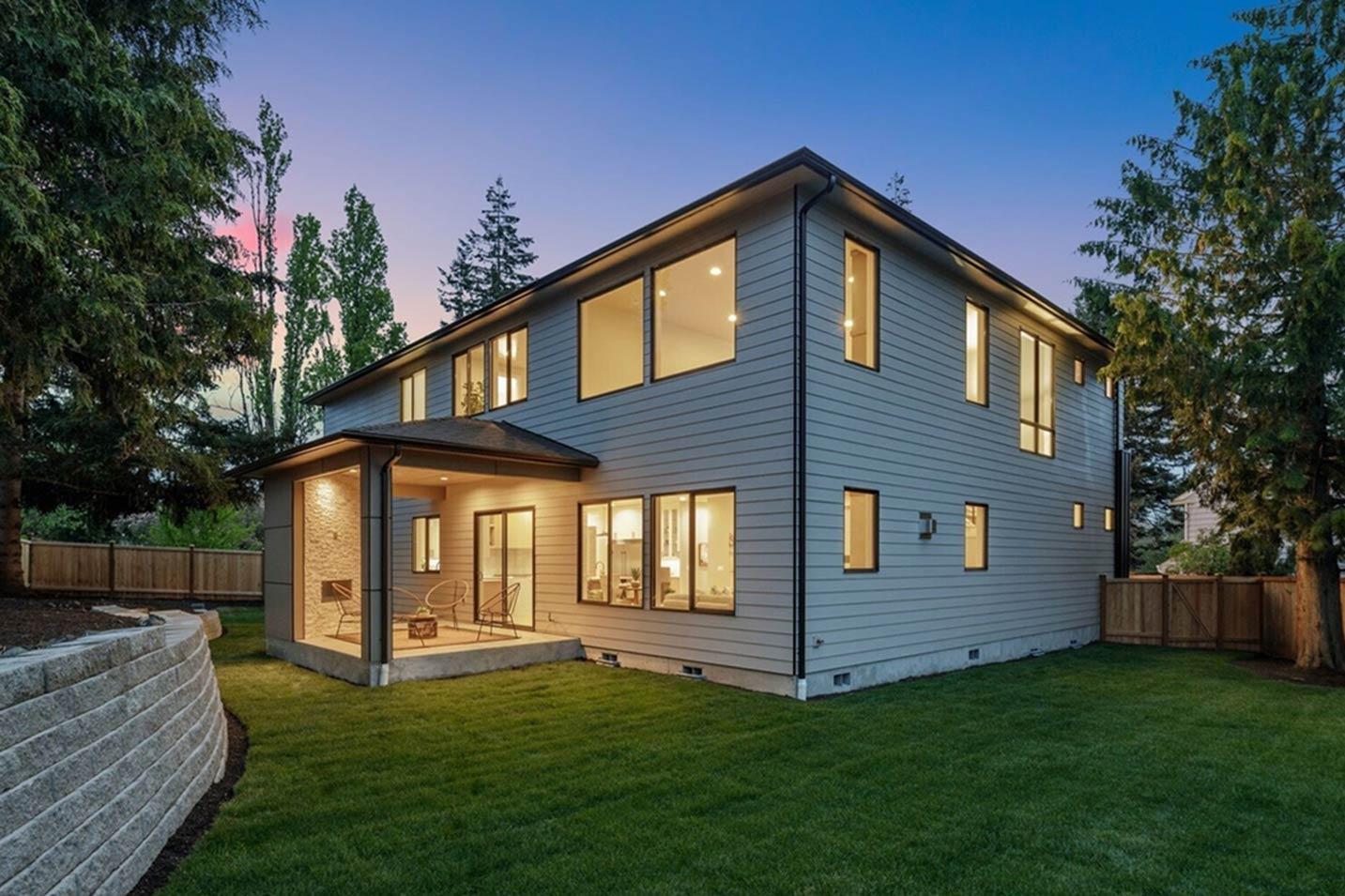 Two-story modern house exterior with horizontal siding, covered patio with stone accent wall, and large windows.