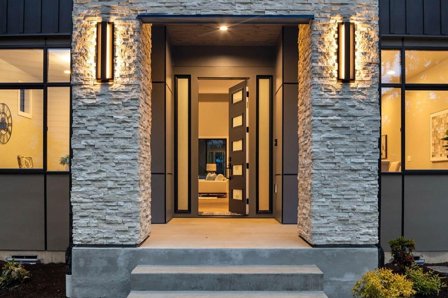 Modern house plan exterior with stacked stone pillars, vertical sconces, and glass-paneled double doors opening to interior.