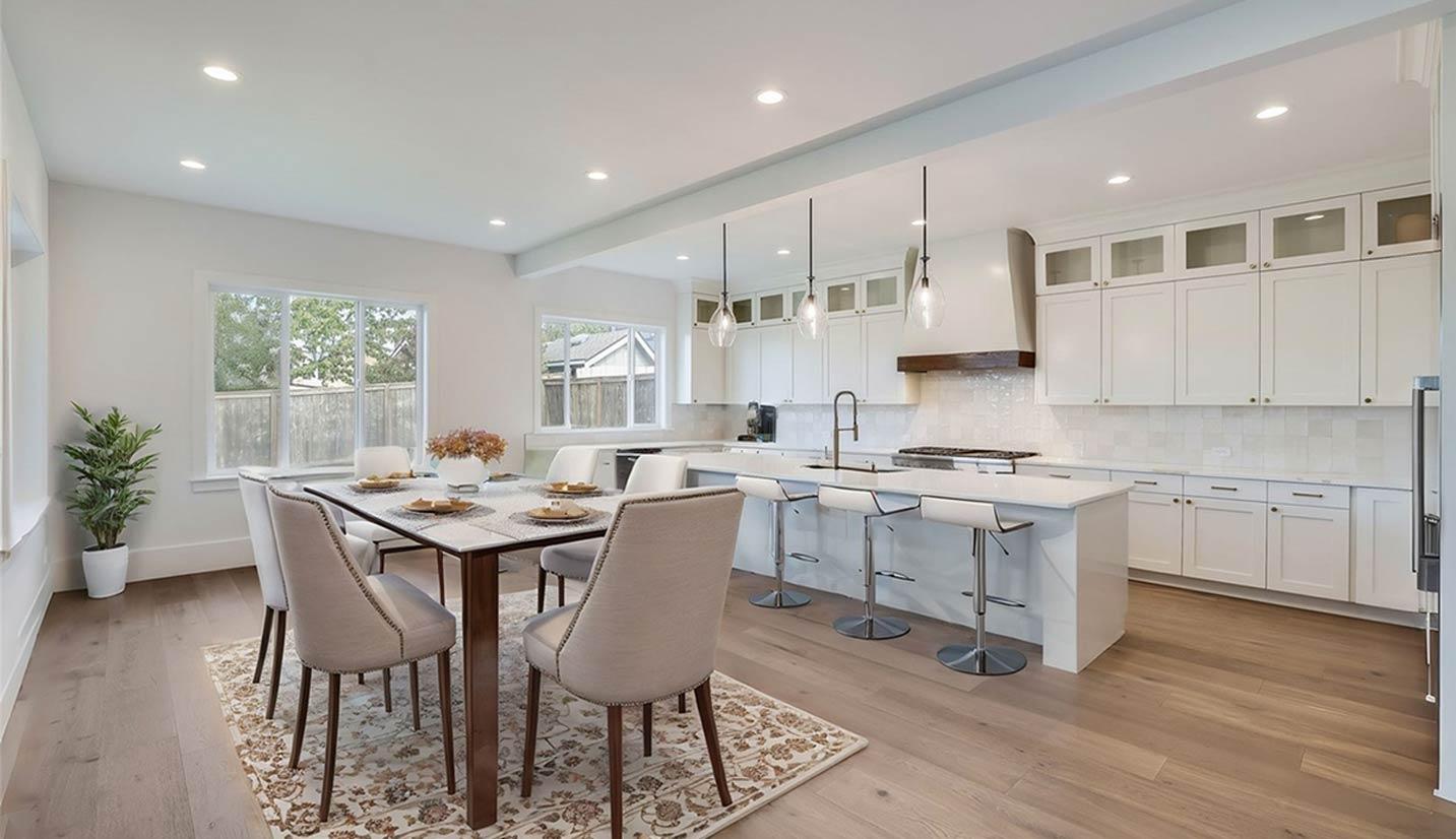Open-concept dining area and kitchen featuring a large island with seating, white cabinetry, and pendant lighting.