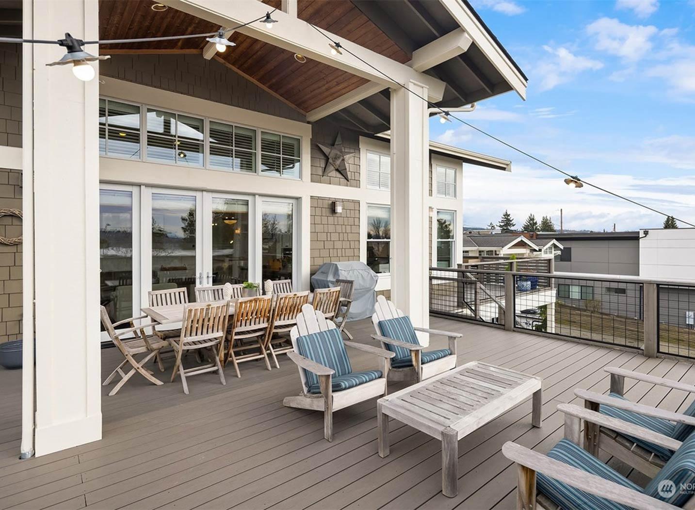 Deck with dining table, chairs, Adirondack chairs, coffee table, and grill under covered roof with exposed beams.