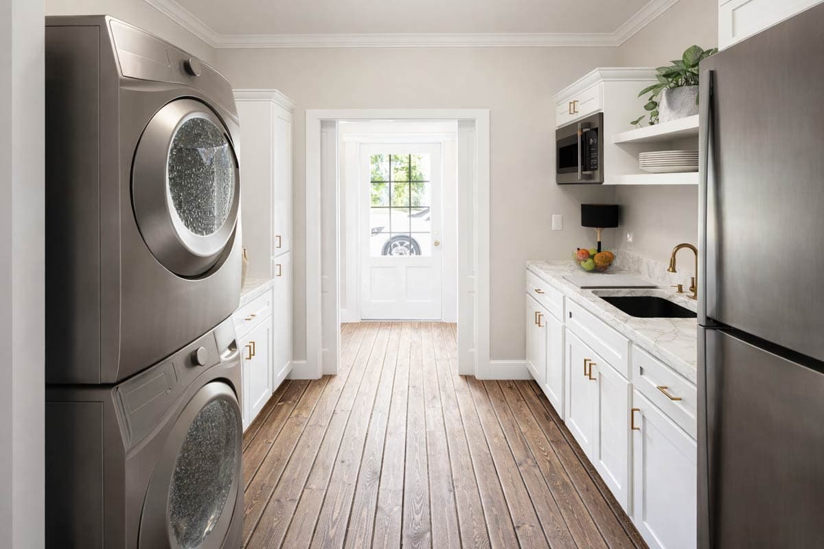Laundry room with stacked washer/dryer, white cabinets, marble counters, stainless steel refrigerator, and door to exterior.