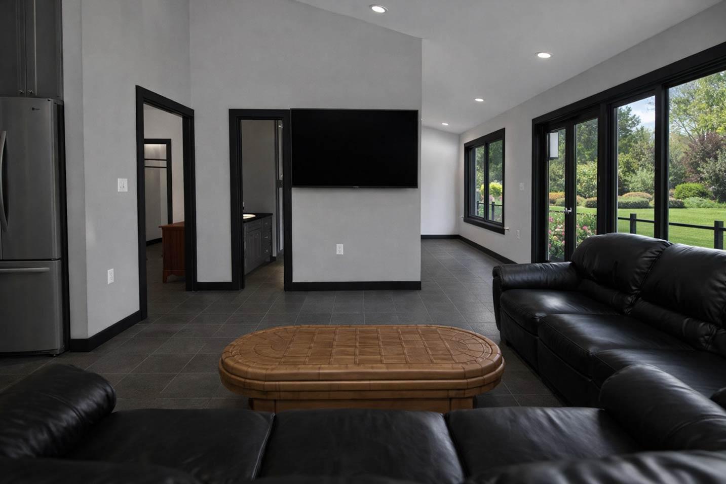 Open concept living space with vaulted ceiling, black framed windows, and a large leather sofa.