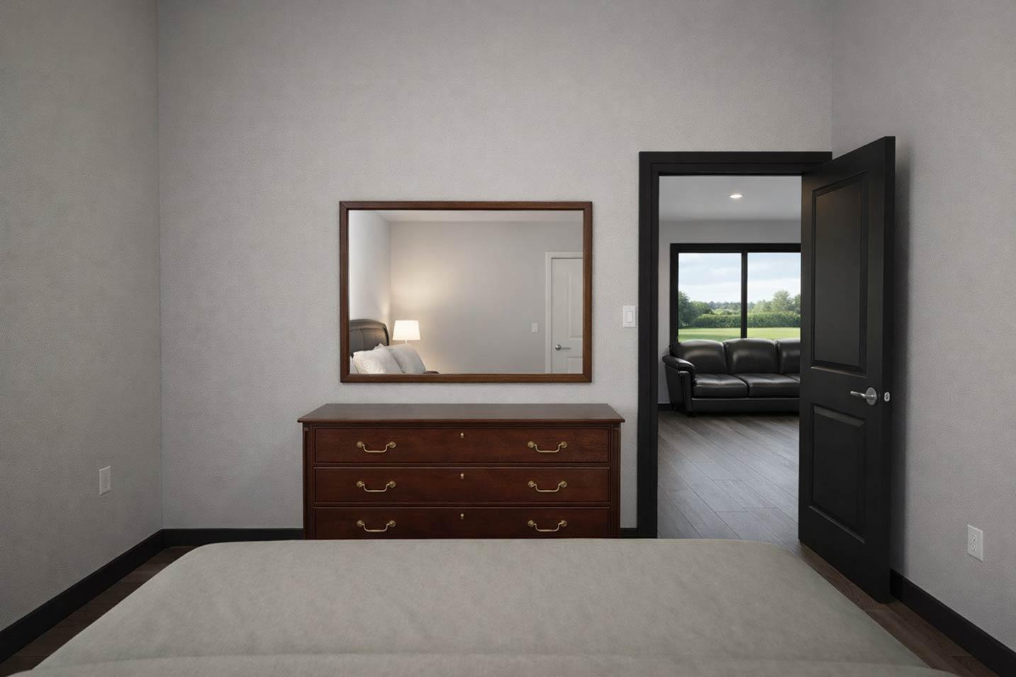 Bedroom with dresser and mirror, doorway opening to living room with sofa and large window.