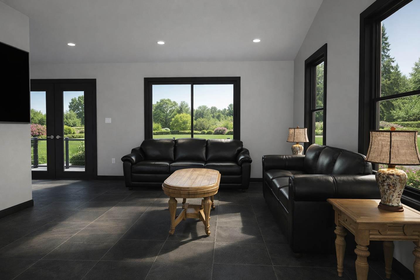 Interior view of a living room with black leather sofas, a wooden coffee table, and large windows overlooking a garden.