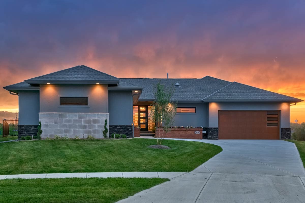 Modern house plan exterior: one-story, stucco finish, hip roof, large driveway, attached garage with wood door.