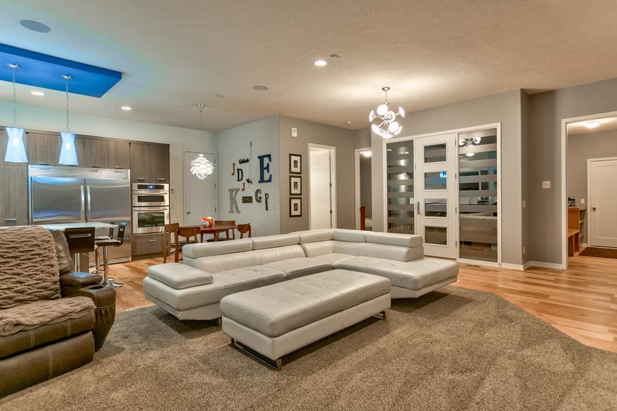 Modern open-concept living area with sectional sofa, dining table, and kitchen with stainless steel appliances.