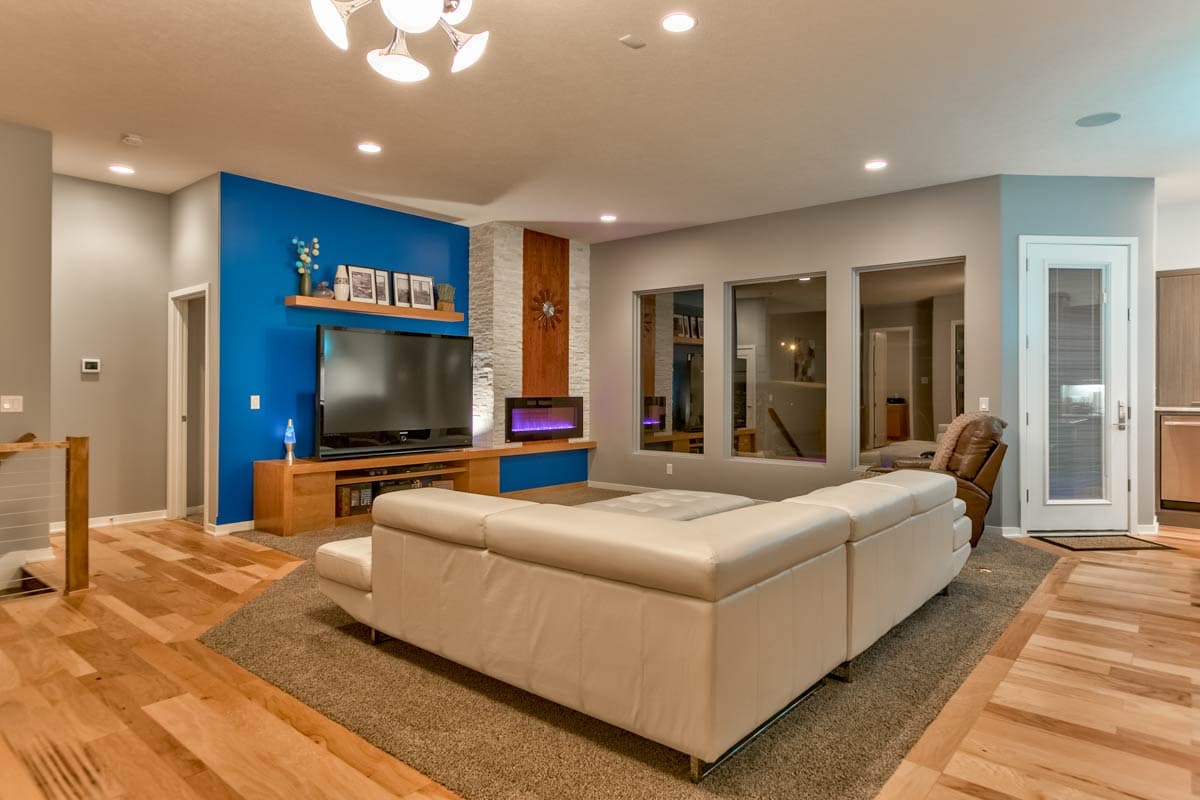 Living room with fireplace, large television on media console, sectional sofa, and three large windows.