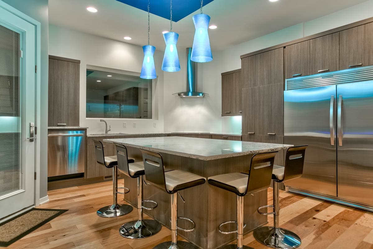 Modern kitchen with island, stainless steel appliances, wood cabinetry, and blue pendant lighting.