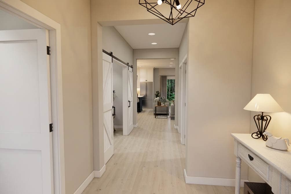 Interior hallway with white doors, including a barn door, leading to a kitchen and living area.