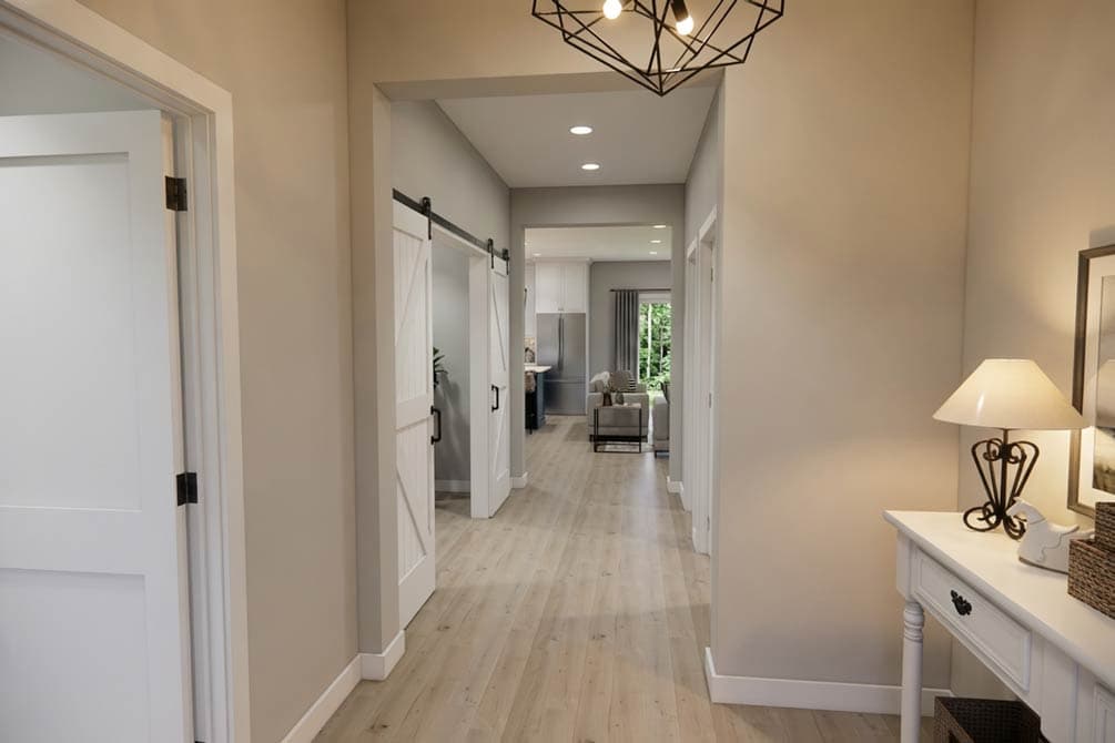 Interior hallway with light wood floors, barn doors, and view into living area and kitchen. Modern light fixture.