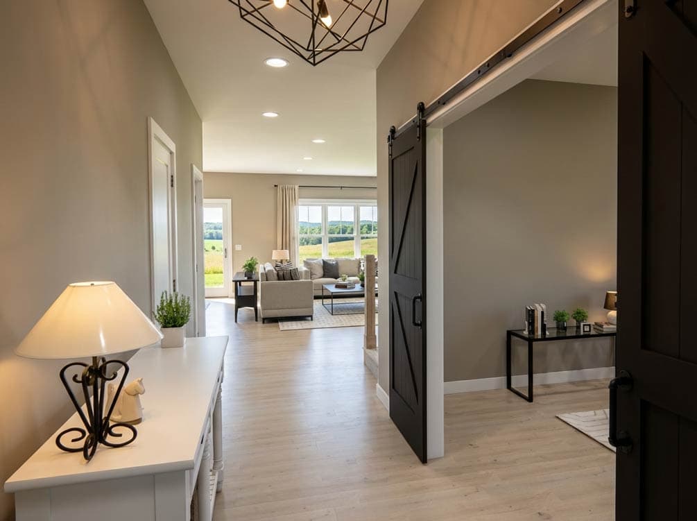 Interior view of a house plan featuring a hallway with a sliding barn door, leading to a living area with large windows and a sofa.