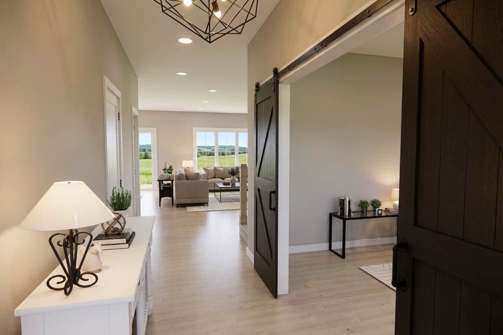 Interior view of a house entryway with a sliding barn door, console table, and open living area beyond with large windows.