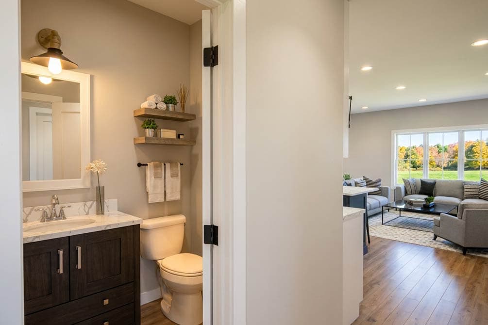 Bathroom with vanity, toilet, and open access to a living area with large windows overlooking a landscape.
