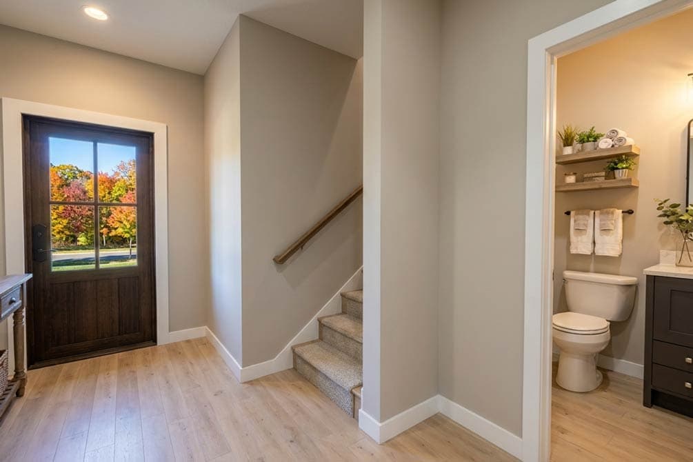 Interior view of a hallway with a wooden door, stairs, and a visible bathroom.