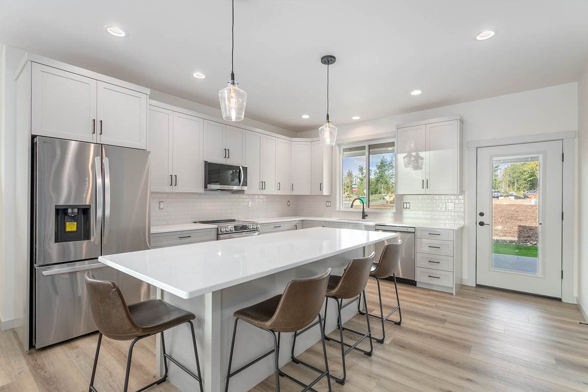 Modern kitchen with white shaker cabinets, quartz island, stainless steel appliances, and glass pendant lights.