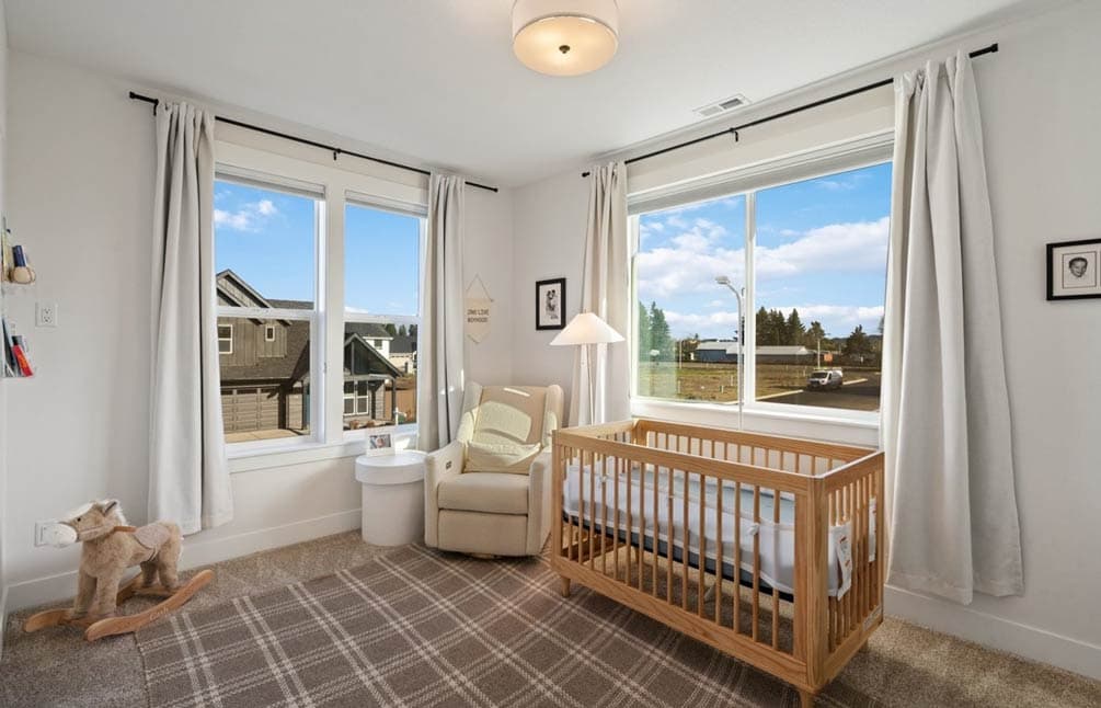 Nursery with a wooden crib, glider, rocking horse, and large windows overlooking houses and a street.