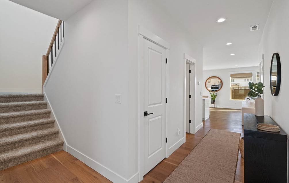 Interior hallway with carpeted stairs, wood floors, white doors, and open view to a living area.