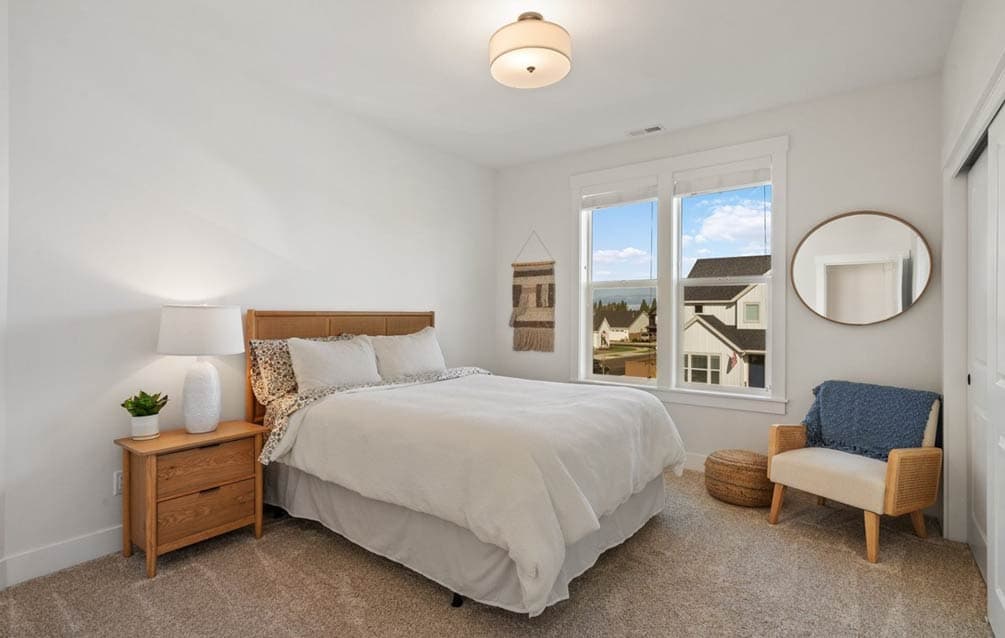 Bedroom with queen bed, nightstand, and large windows overlooking neighborhood houses.