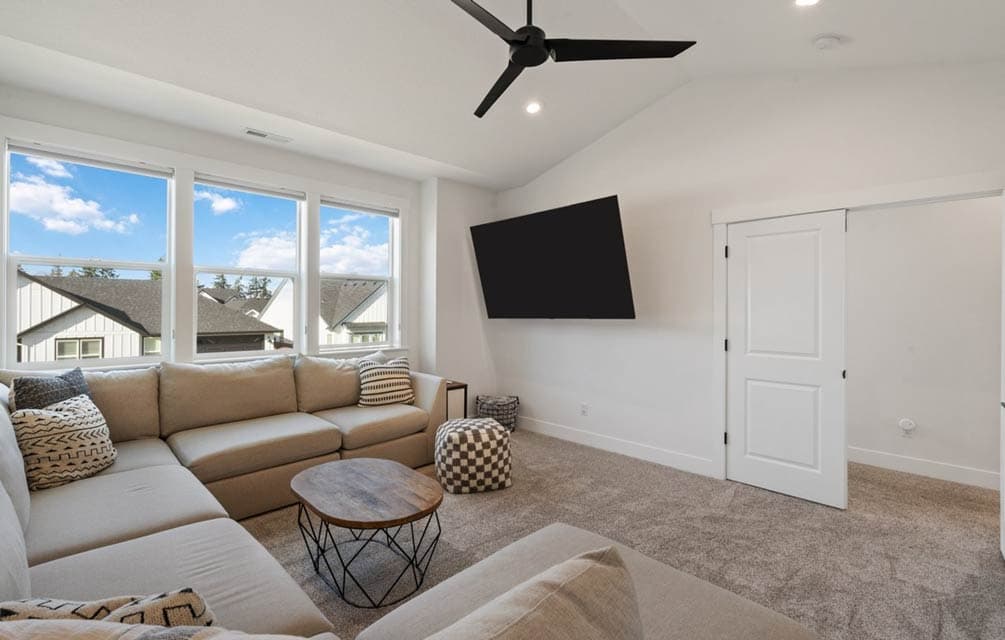 Interior view of living area with sectional sofa, large windows, ceiling fan, and mounted TV.