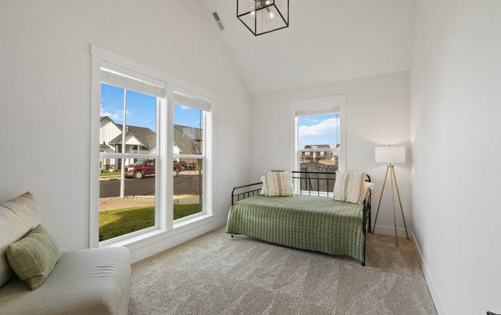 Interior view of a bedroom with a daybed, large windows, and a vaulted ceiling. Visible homes outside.