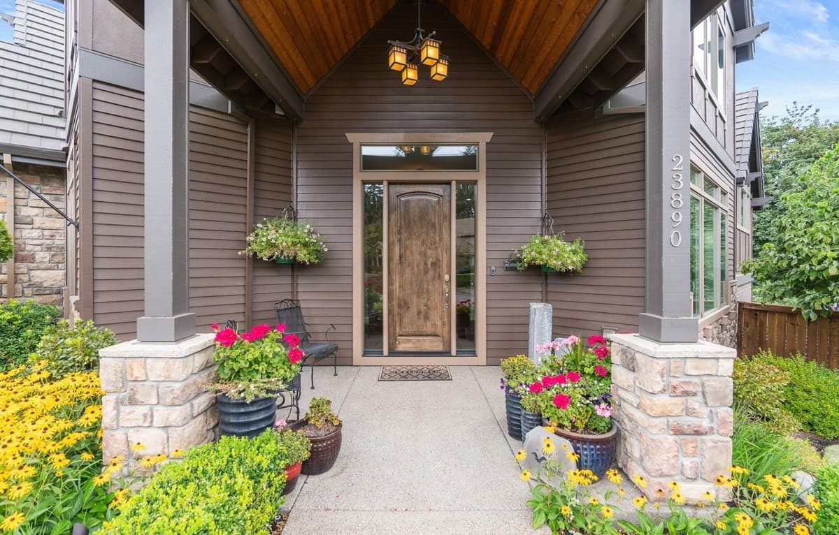 House plan exterior with covered entry, wood door, stone column bases, and side gables.