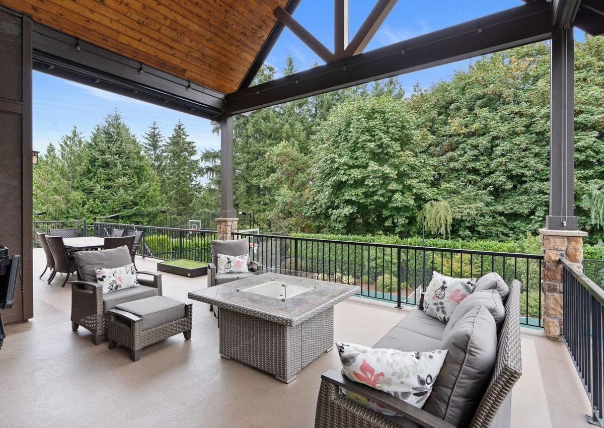 Covered outdoor living space with seating, fire pit, and dining area, featuring a wood-paneled ceiling and exposed beams.