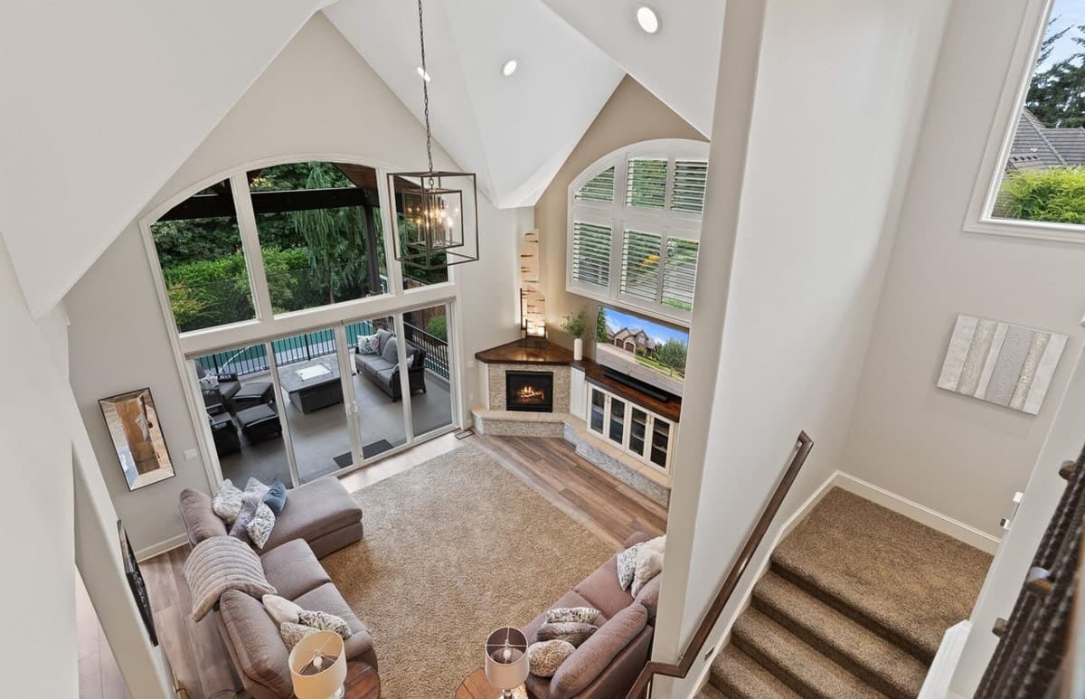 Great room with vaulted ceiling, corner fireplace, large windows overlooking patio, and staircase.