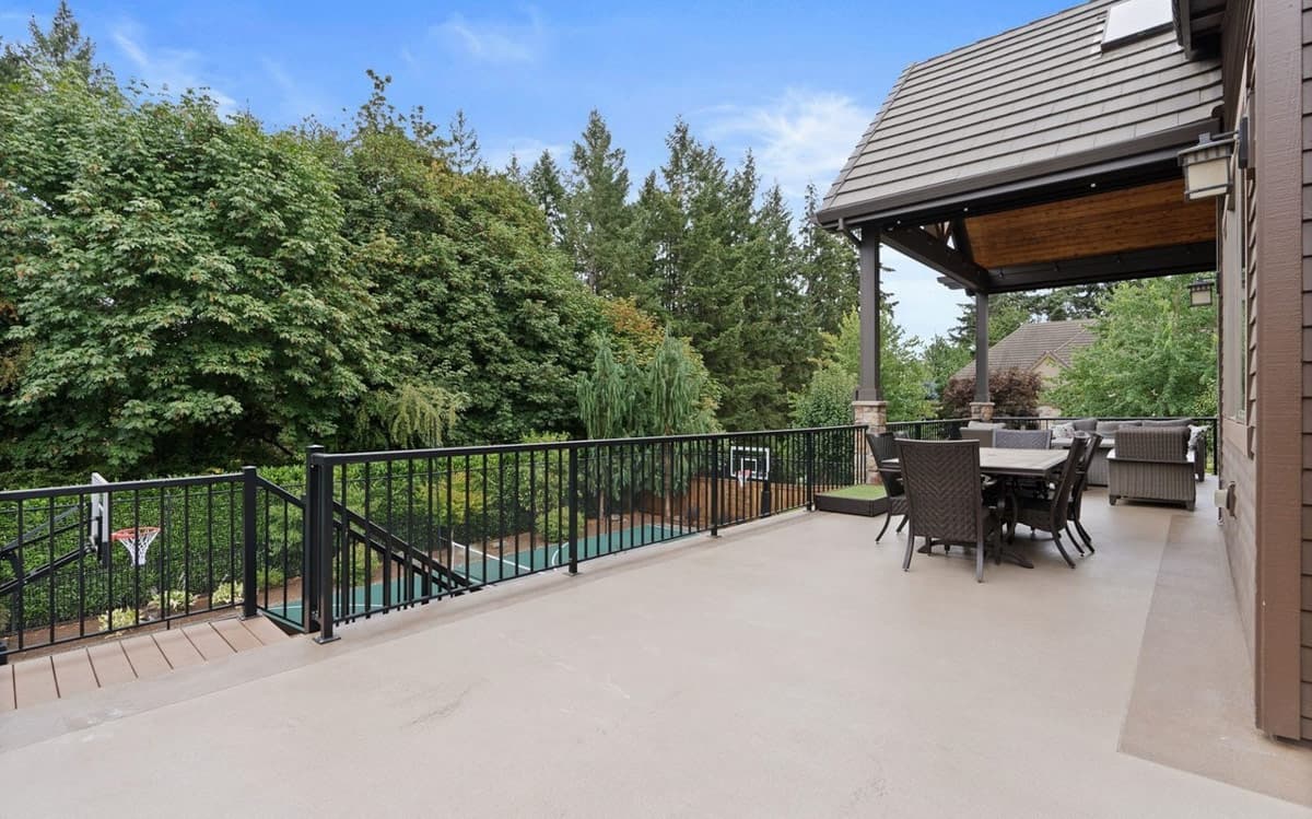 Exterior view of house plan with large covered deck, outdoor dining, basketball court, and wooded background.