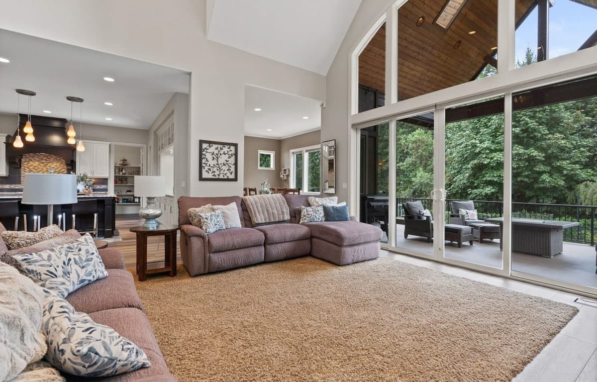 Interior view of a living room with vaulted ceilings, a sectional sofa, and large sliding glass doors opening to a deck.