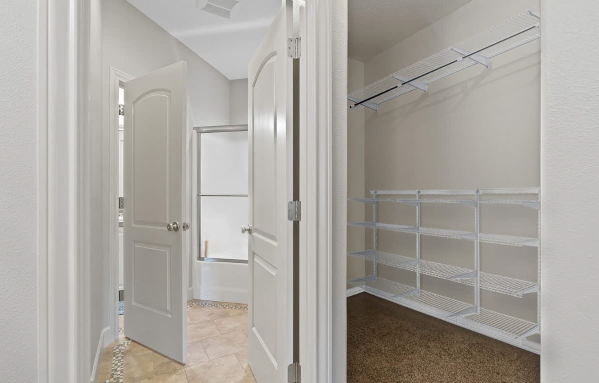 Hallway with open doors revealing a bathroom with a shower and a walk-in closet with wire shelving.