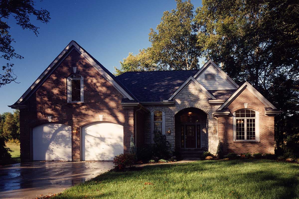 House plan exterior with a brick facade, two garage doors, stone arched entryway, and multiple gables.