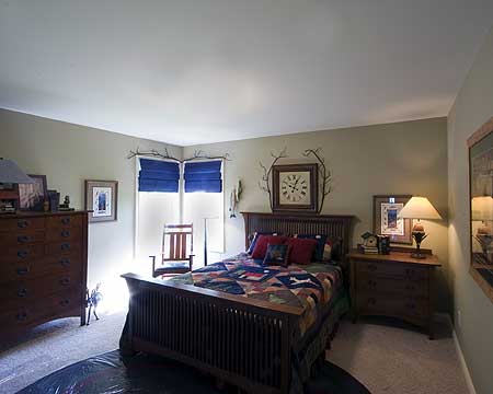 Bedroom with wooden bed, quilt, dresser, rocking chair, and clock.