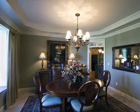Dining room with wood table, chairs, buffet, painting, and chandelier. Tray ceiling with crown molding.