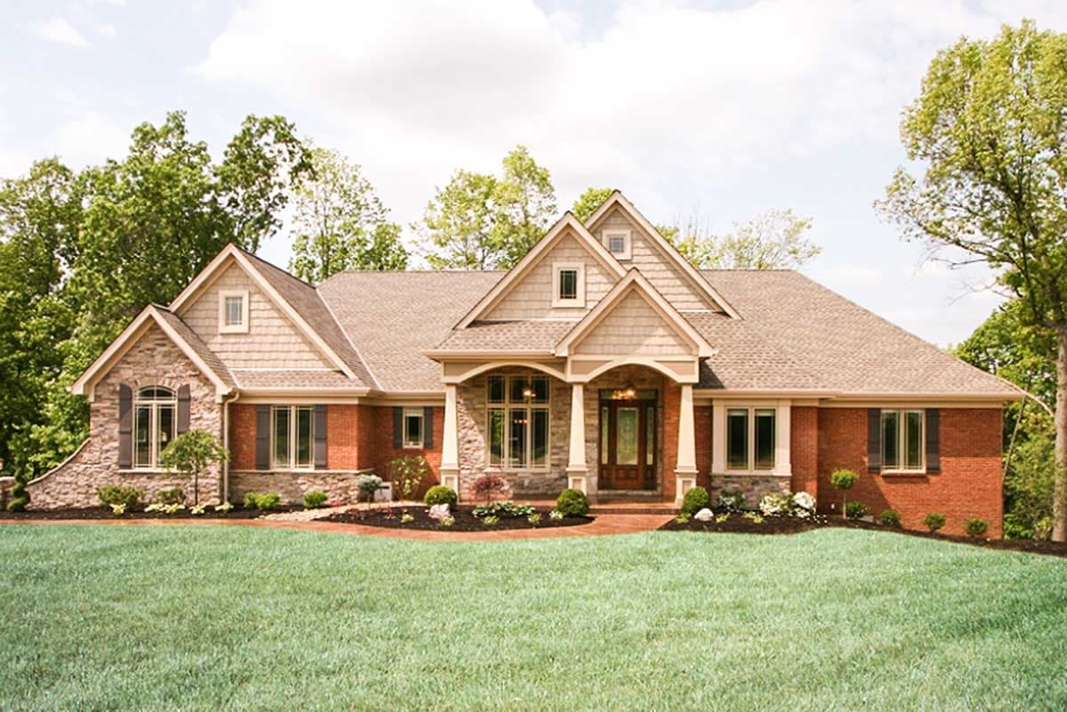 House plan exterior. One-story Ranch style home with gables, stone and brick facade, and a covered porch. Features multiple dormers.