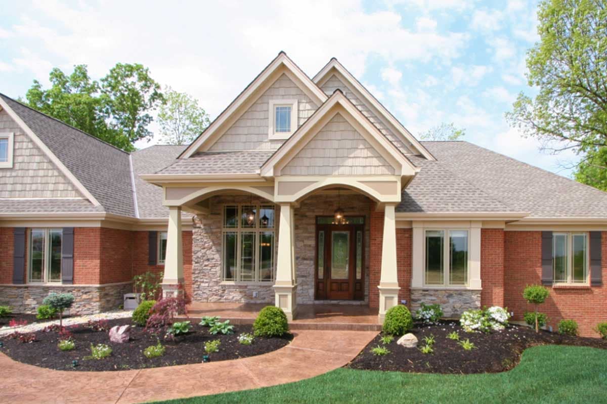 House plan exterior: Craftsman style, one-story, brick with stone accents, arched entry porch with decorative columns.