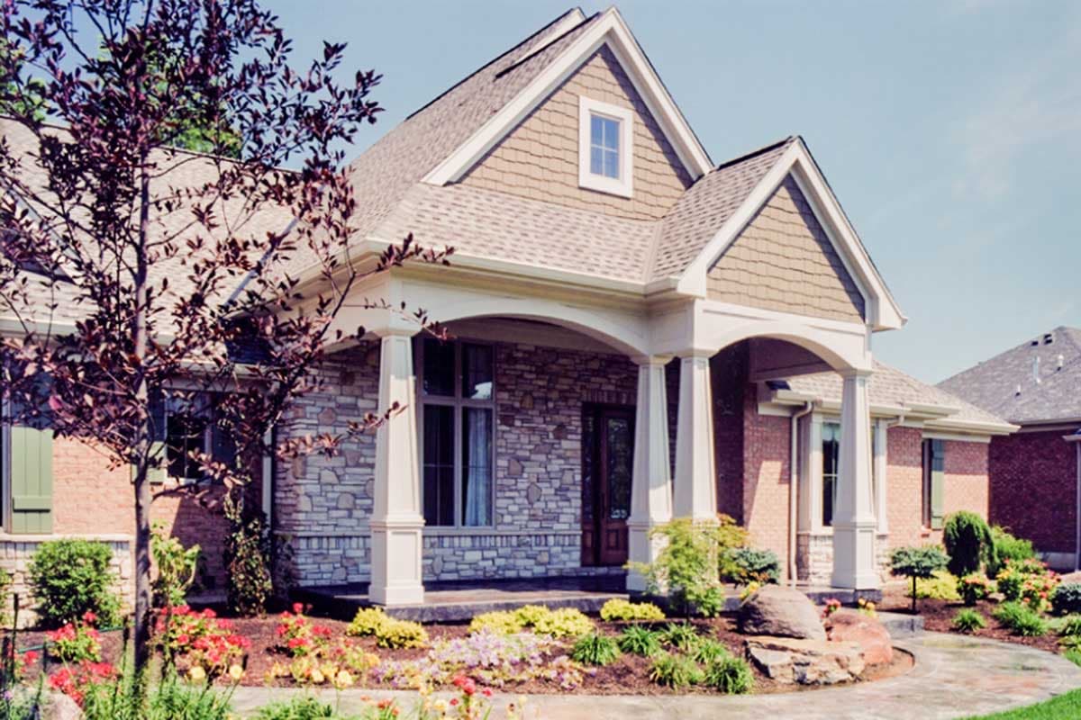 House plan exterior: Two-story home with arched entryway, stone accents, gables, and dormer.