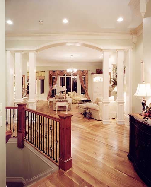Interior view showing a staircase with ornate balusters leading to a living area with columns, an arched entryway, and plush seating.