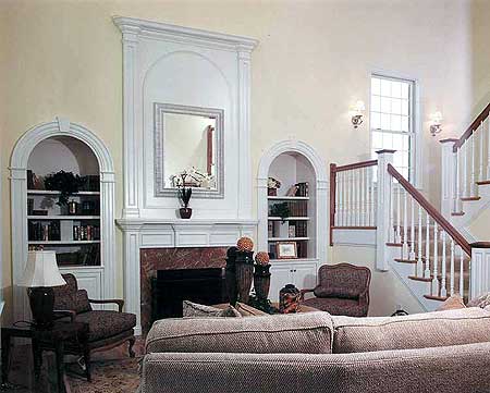 Living room with fireplace, arched built-in bookshelves, and a staircase with white balusters.