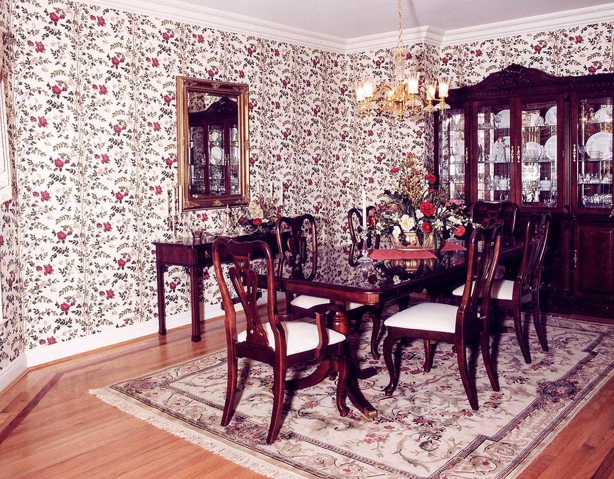Dining room with floral wallpaper, wood table and chairs, buffet cabinet, and ornate rug.
