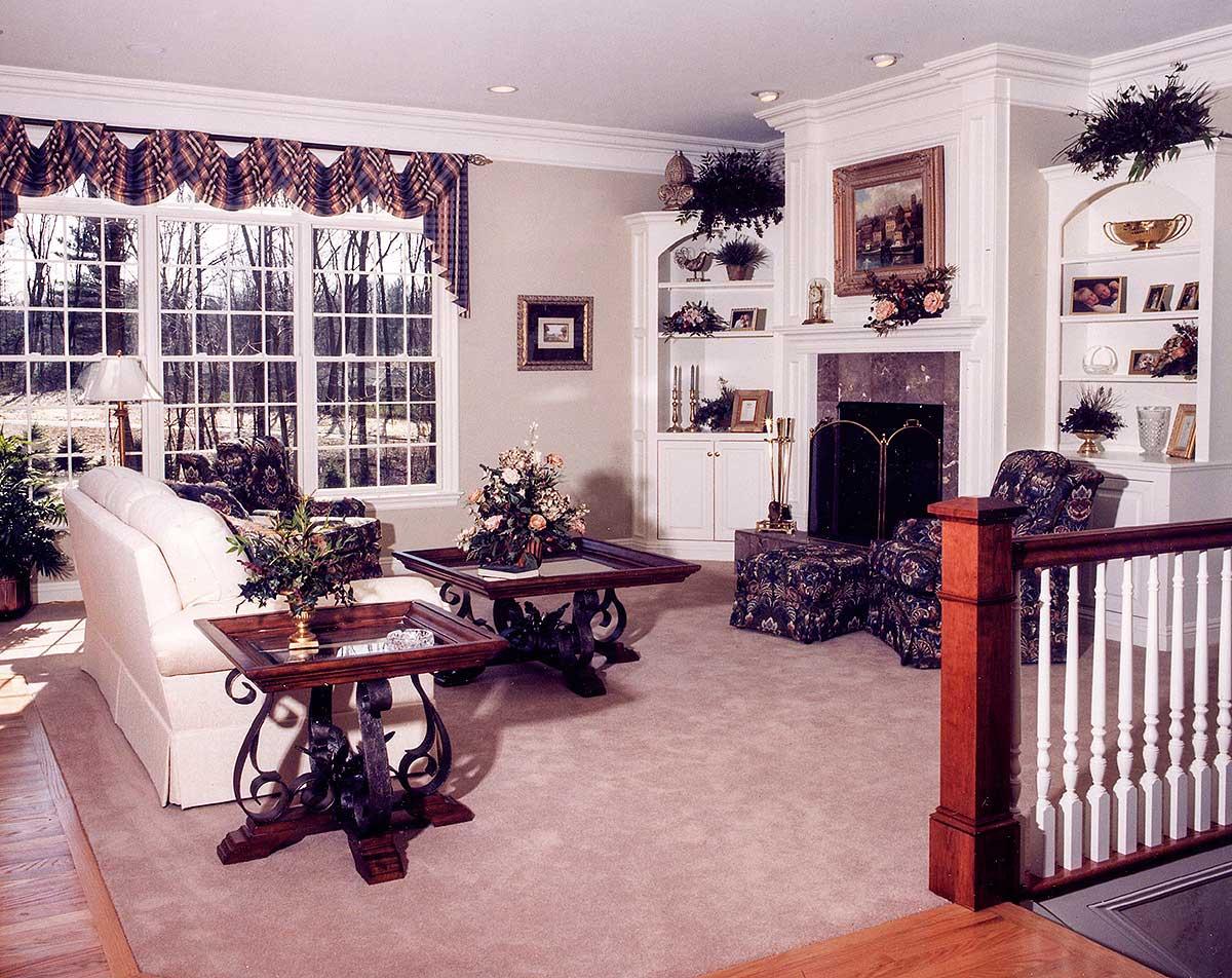 Living room interior with fireplace, built-in bookshelves, large windows, and upholstered seating.