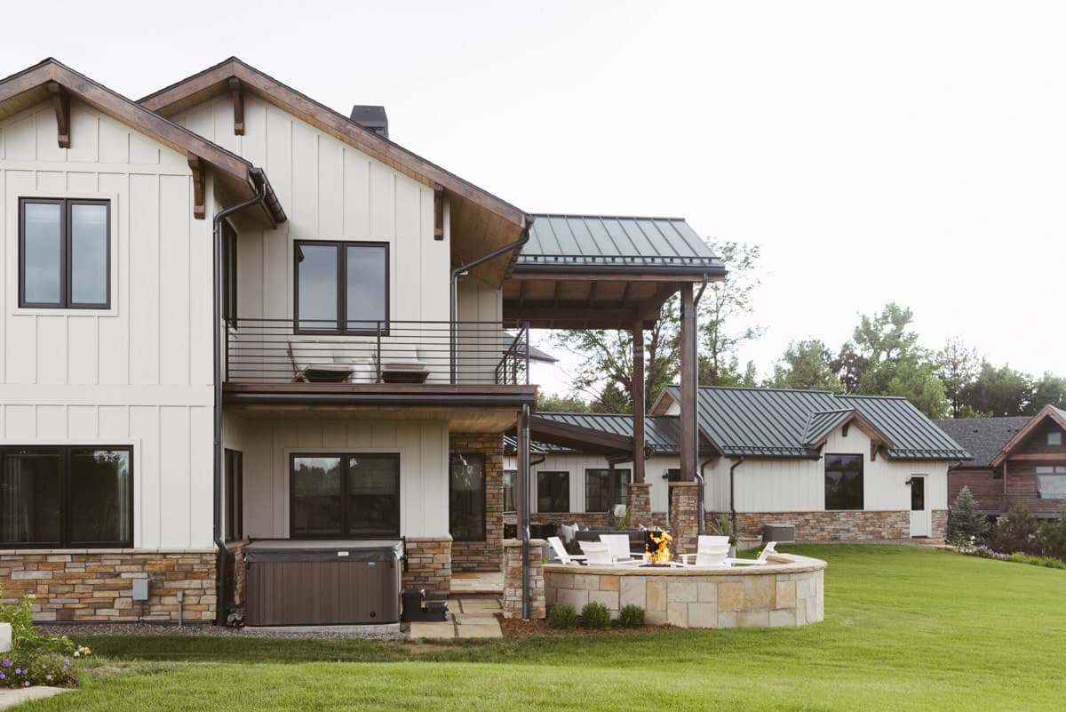Modern farmhouse house plan exterior with board-and-batten siding, stone accents, multiple gables, and a covered outdoor living area with fire pit.