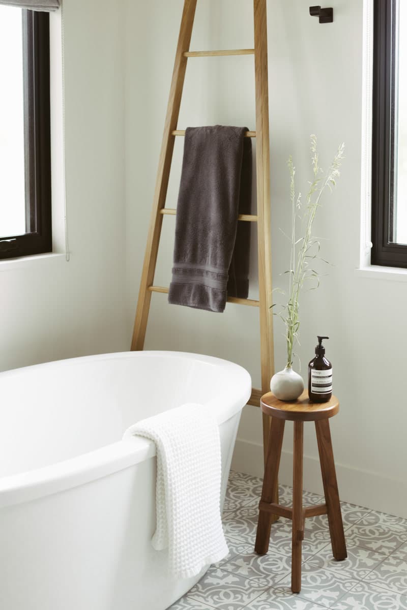 Modern bathroom interior with freestanding tub, wooden ladder towel rack, and patterned tile floor.
