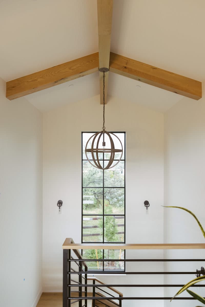 Interior view with vaulted ceiling, exposed wood beams, large grid window, and pendant light.