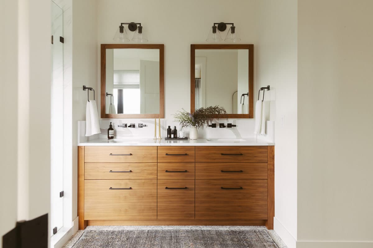 Bathroom vanity with two sinks, wood cabinetry, white quartz countertops, and modern sconce lighting.
