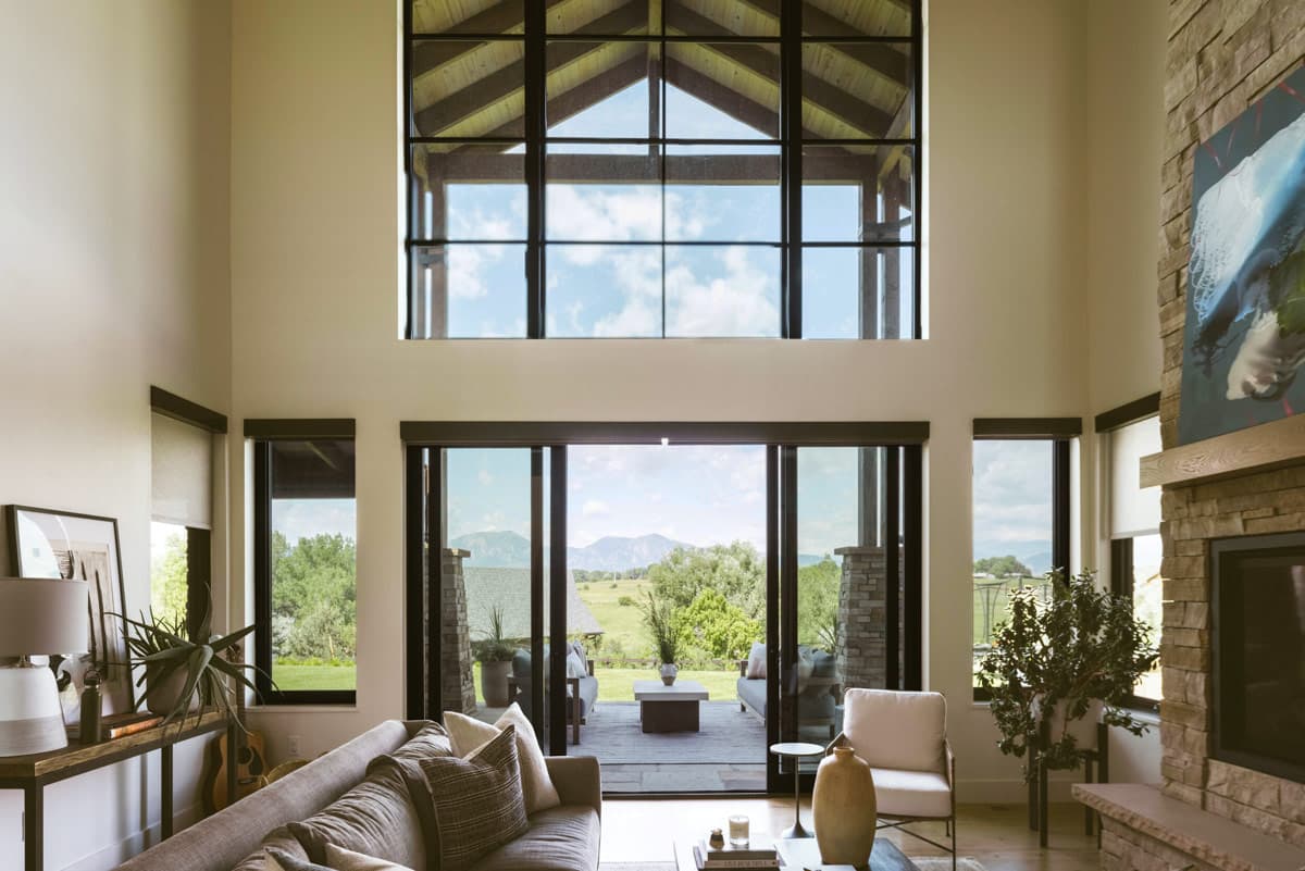 Great room with vaulted ceiling, large windows, sliding glass doors to patio, and stone fireplace.