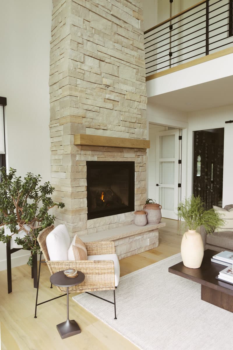 Great room with stacked stone fireplace, wood mantel, and a view of the loft with black metal railing.